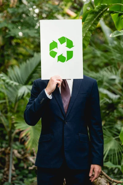 Homme d'affaires tenant une carte avec panneau de recyclage vert devant le visage en serre — Photo de stock