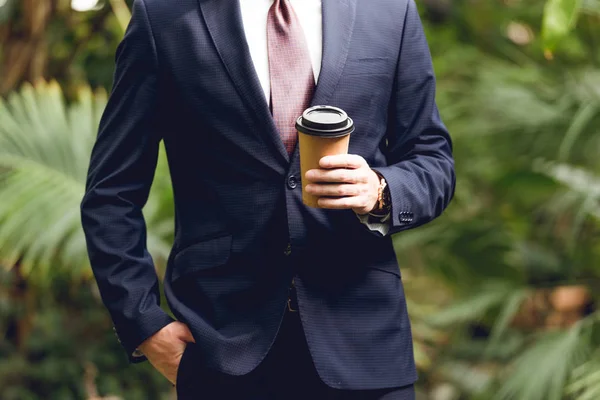 Cropped view of businessman in suit and tie holding coffee to go in orangery — Stock Photo