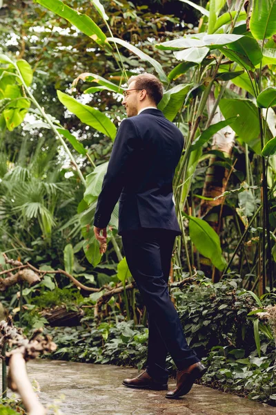 Happy businessman in suit talking on smartphone while walking in greenhouse — Stock Photo