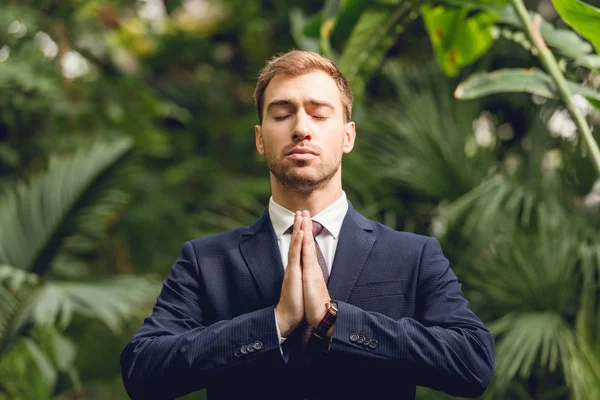 Handsome businessman in suit and tie with closed eyes meditating in orangery — Stock Photo