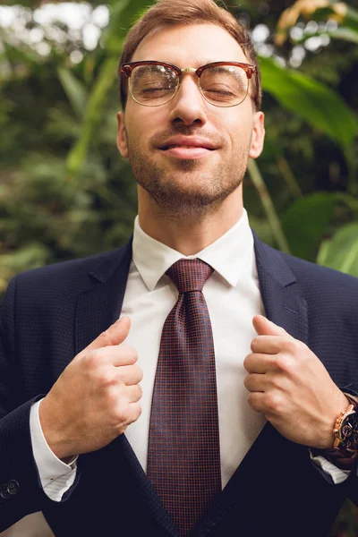 Handsome businessman in suit and glasses with closed eyes breathing fresh air in orangery — Stock Photo