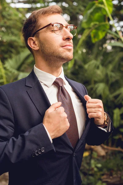 Businessman in suit and glasses with closed eyes breathing fresh air in orangery — Stock Photo