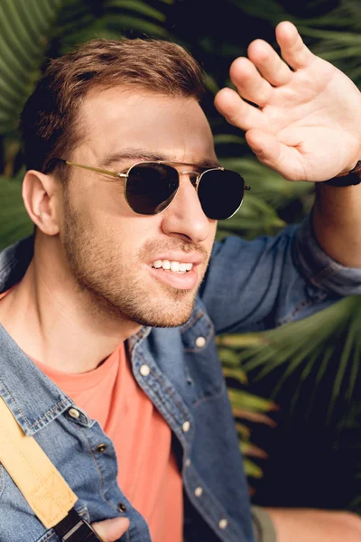 Beau touriste dans des lunettes de soleil mettant la main contre le soleil — Photo de stock