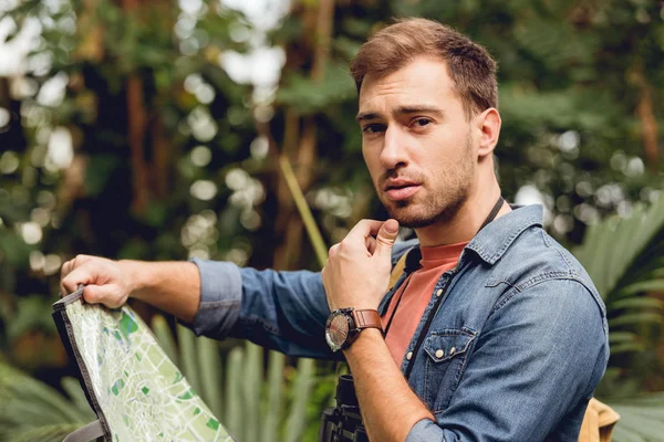 Beau voyageur songeur tenant carte dans la forêt tropicale verte — Photo de stock