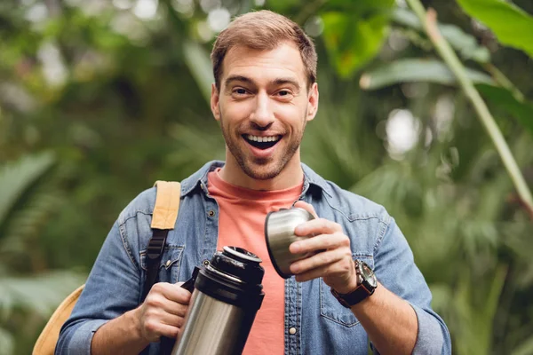 Voyageur heureux avec sac à dos ouverture thermos en forêt tropicale — Photo de stock