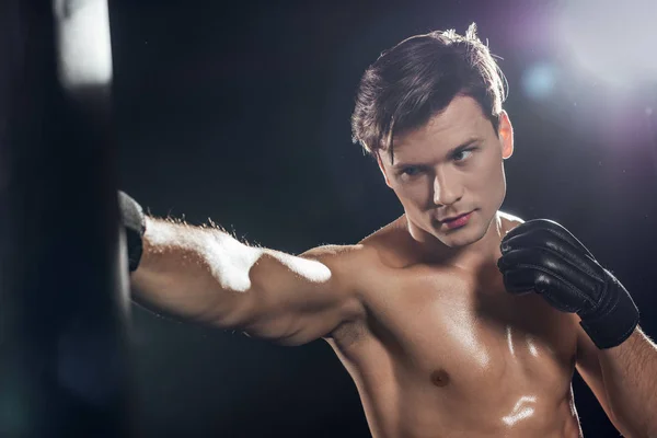Handsome boxer in boxing gloves training with punching bag on black — Stock Photo