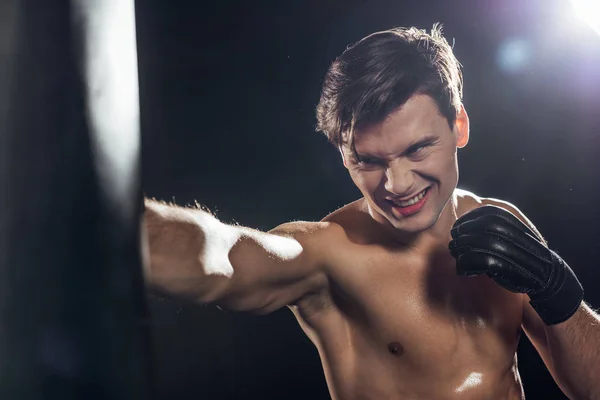 Handsome boxer in boxing glove training with punching bag on black — Stock Photo