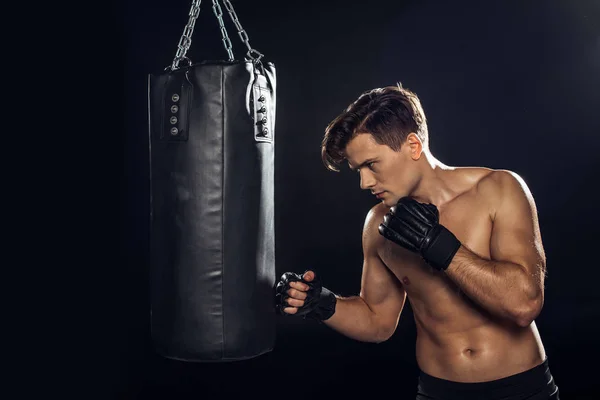 Handsome boxer in boxing gloves training with punching bag on black — Stock Photo