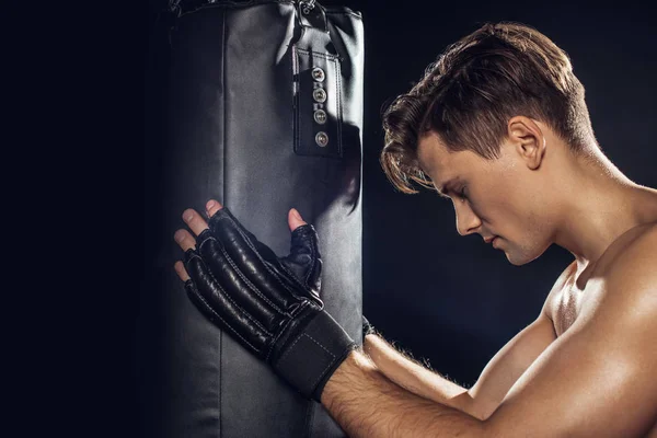 Боковой вид боксера, держащего боксерскую грушу с закрытыми глазами на черном — стоковое фото