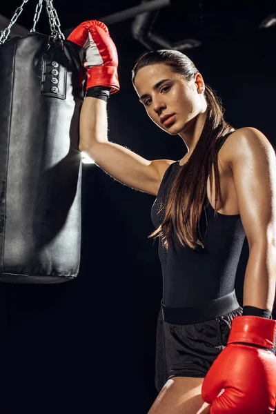 Boxer donna in guanti da boxe rossi in piedi vicino al sacco da boxe — Foto stock