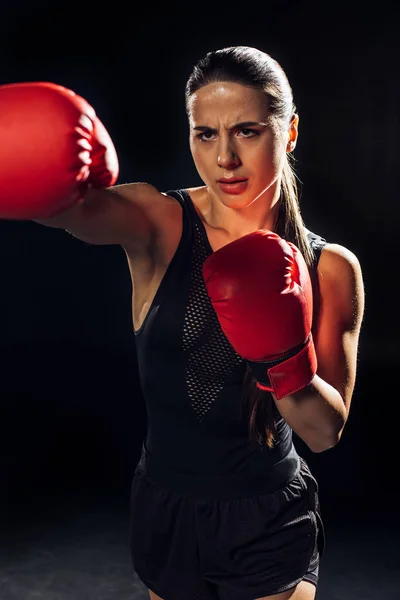 Focused female boxer in red boxing gloves training and looking away on black — Stock Photo