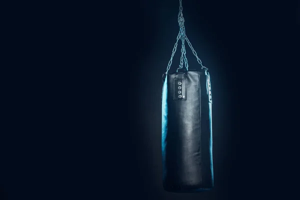 Leather punching bag hanging on steel chains on black — Stock Photo