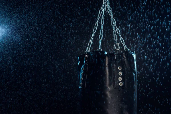 Leather punching bag hanging on steel chains under water drops on black — Stock Photo