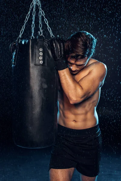 Exhausted boxer in black briefs holding punching bag and looking down on black — Stock Photo