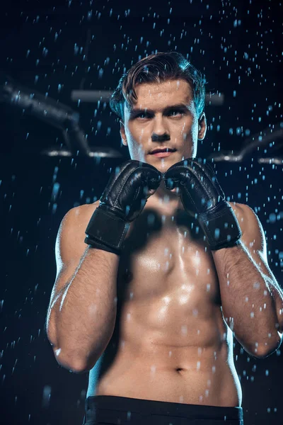 Pensive boxer in leather gloves standing under water drops and looking away — Stock Photo