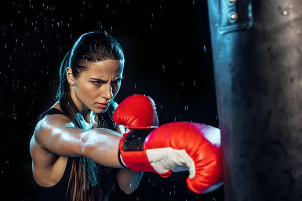 Pensive boxer in red boxing gloves training under water drops on black — Stock Photo