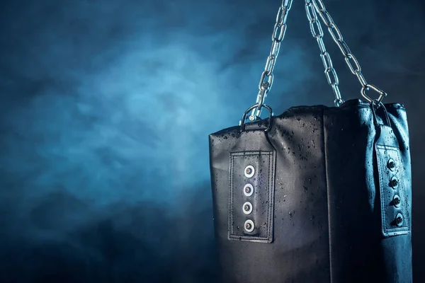 Leather punching bag hanging on steel chains on dark — Stock Photo