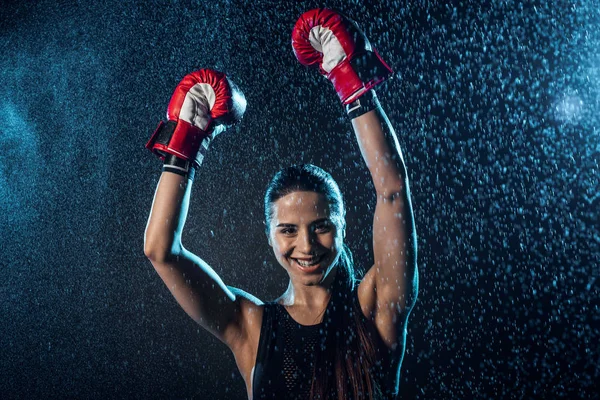 Smiling boxer in red boxing gloves showing yes gesture under water drops on black — Stock Photo