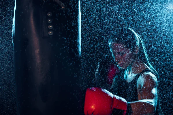 Boxer fort en gants de boxe rouge s'entraînant sous l'eau gouttes sur noir — Photo de stock