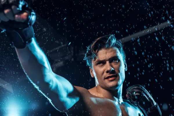 Tiefansicht eines Boxers in Lederhandschuhen, der unter Wassertropfen auf schwarz steht — Stockfoto
