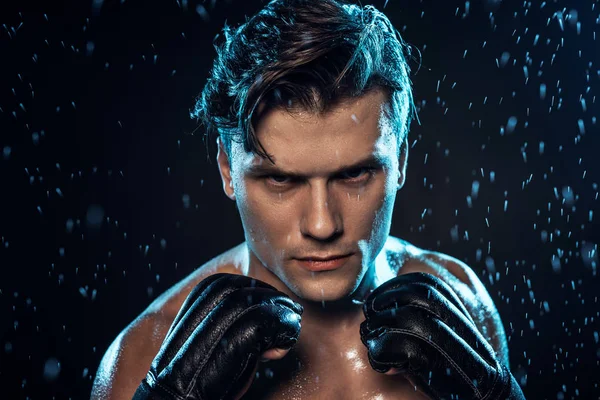 Front view of boxer in leather gloves standing under water drops on black — Stock Photo