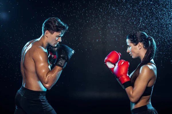 Side view of two boxers in boxing gloves training together under water drops on black — Stock Photo
