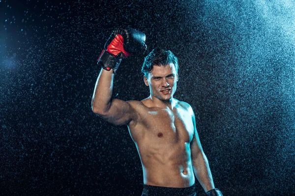 Smiling boxer standing with hand up under water drops on black — Stock Photo