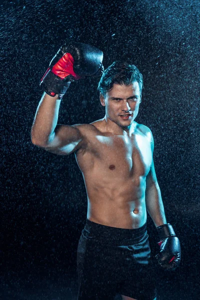 Smiling boxer standing with hand up under water drops on black — Stock Photo