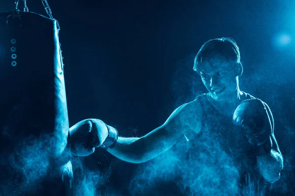 Aggressive boxer in boxing gloves training with punching bag — Stock Photo