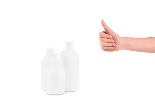 Vista parcial da mulher com garrafas de cosméticos mostrando polegar para cima isolado em branco — Fotografia de Stock