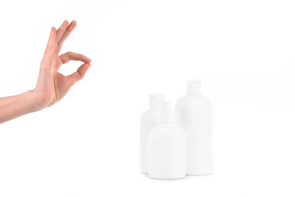 Cropped view of girl with cosmetic bottles showing okay sign isolated on white — Stock Photo