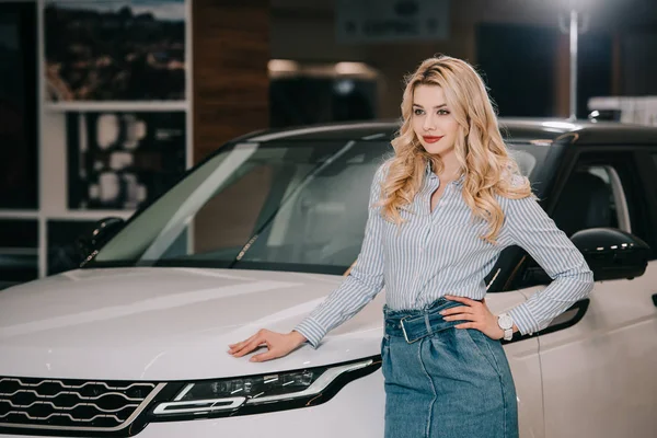 Счастливая блондинка, стоящая с рукой на бедре возле белого автомобиля — стоковое фото