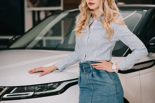 Vista ritagliata di ragazza bionda in piedi con mano sul fianco vicino automobile bianca — Foto stock