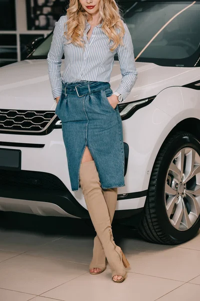 Обрізаний вид блондинки, що стоїть з руками в кишенях біля білої машини — стокове фото