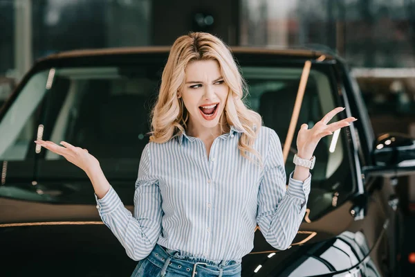 Attractive blonde woman screaming and gesturing near black car — Stock Photo
