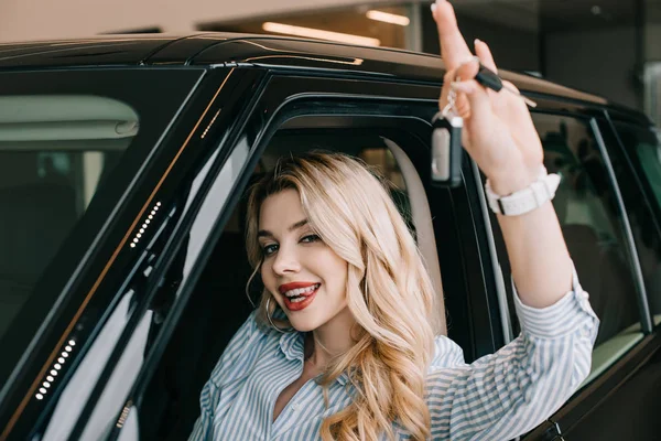 Selective focus of happy young woman holding car key while sitting in automobile — Stock Photo