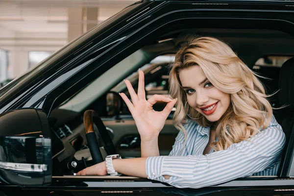 Heureuse jeune femme assise dans la voiture et montrant ok signe — Photo de stock