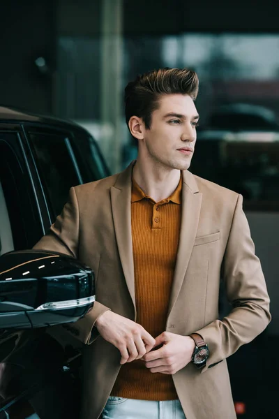 Bonito homem de pé perto de preto automóvel no carro showroom — Fotografia de Stock