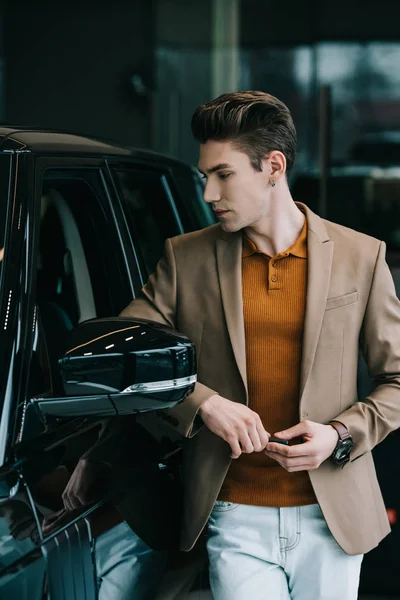 Bel homme regardant l'automobile noire dans la salle d'exposition de voiture — Photo de stock