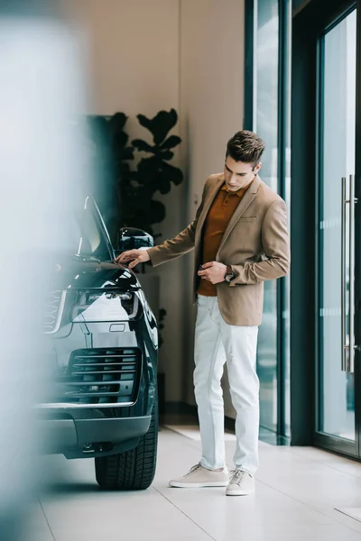 Foco seletivo de homem bonito olhando para o automóvel preto no showroom do carro — Fotografia de Stock