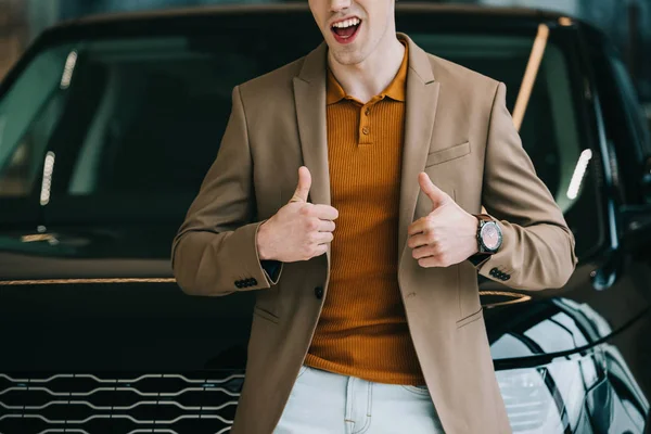 Vue recadrée de l'homme joyeux debout près de l'automobile et montrant pouces vers le haut — Photo de stock