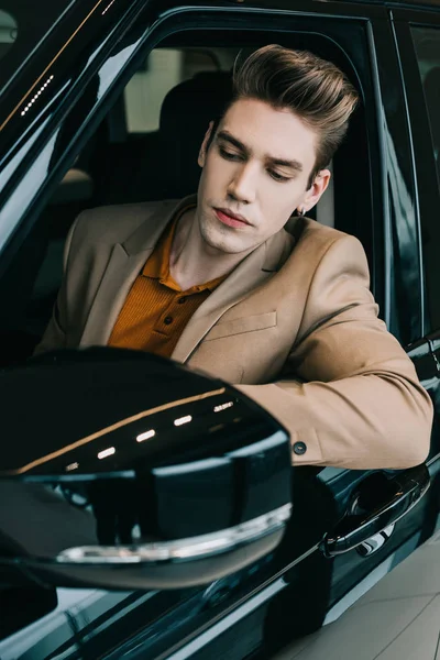 Hombre guapo sentado en el automóvil en sala de exposición de coches - foto de stock