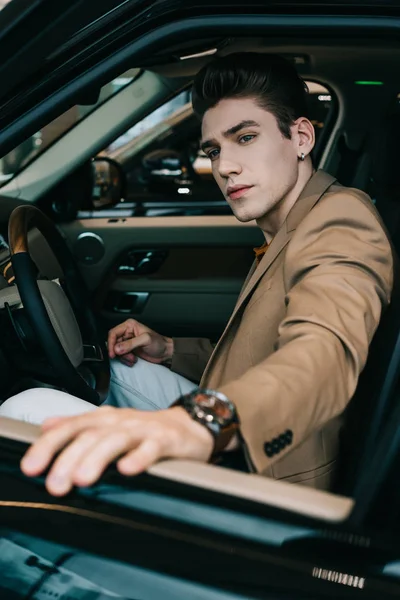 Selective focus of handsome man sitting in automobile in car showroom — Stock Photo