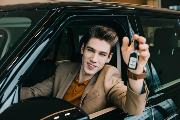 Foco seletivo do homem feliz segurando a chave do carro enquanto sentado no automóvel — Fotografia de Stock