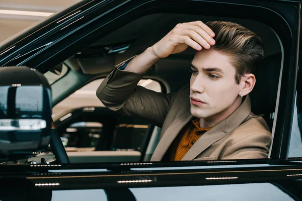Hombre guapo tocando el pelo mientras está sentado en el coche - foto de stock