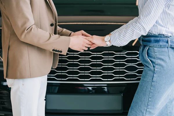 Cropped view of man and woman holding hands near automobile — Stock Photo