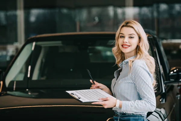 Веселый дилер автомобилей блондинка держит планшет с контрактом и ручкой — стоковое фото