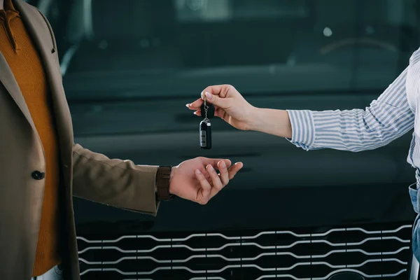 Cropped view of car dealer giving key to man in car showroom — Stock Photo