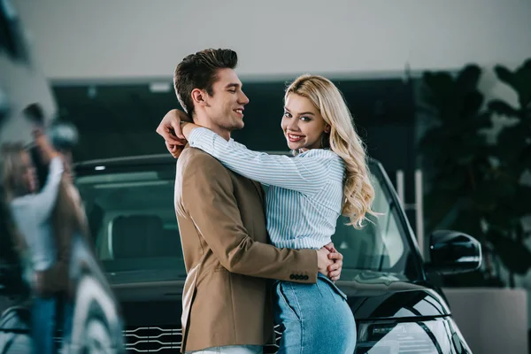 Красива блондинка обіймає щасливого чоловіка, стоячи біля машини — стокове фото