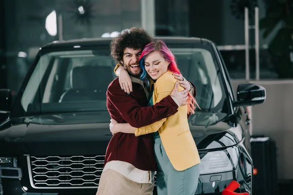 Homem encaracolado alegre abraçando menina feliz com cabelo colorido — Stock Photo